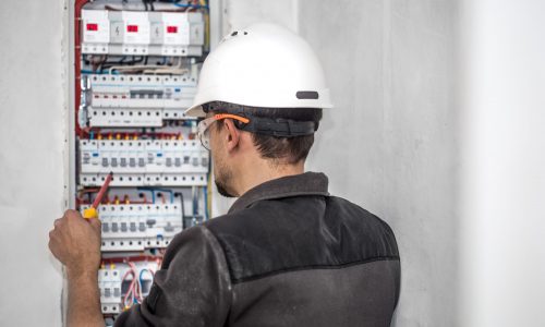 Man, an electrical technician working in a switchboard with fuses. Installation and connection of electrical equipment. Professional with tools in hand. concept of complex work, space for text.